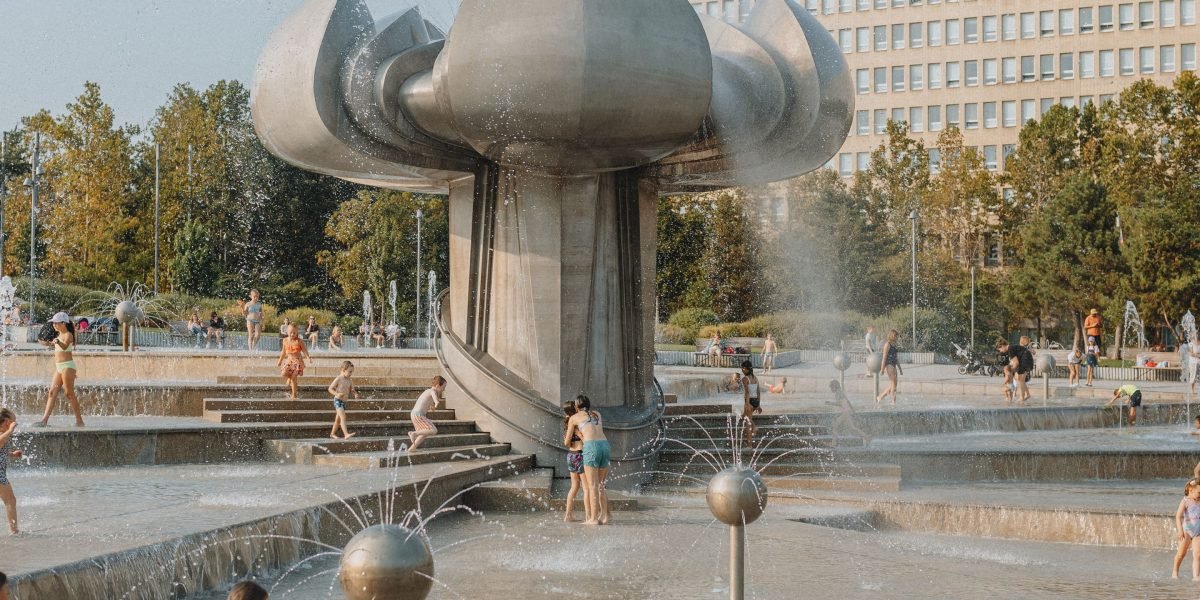 People enjoying an evening stroll near a grand illuminated fountain and modern architecture, capturing the vibrant downtown atmosphere.