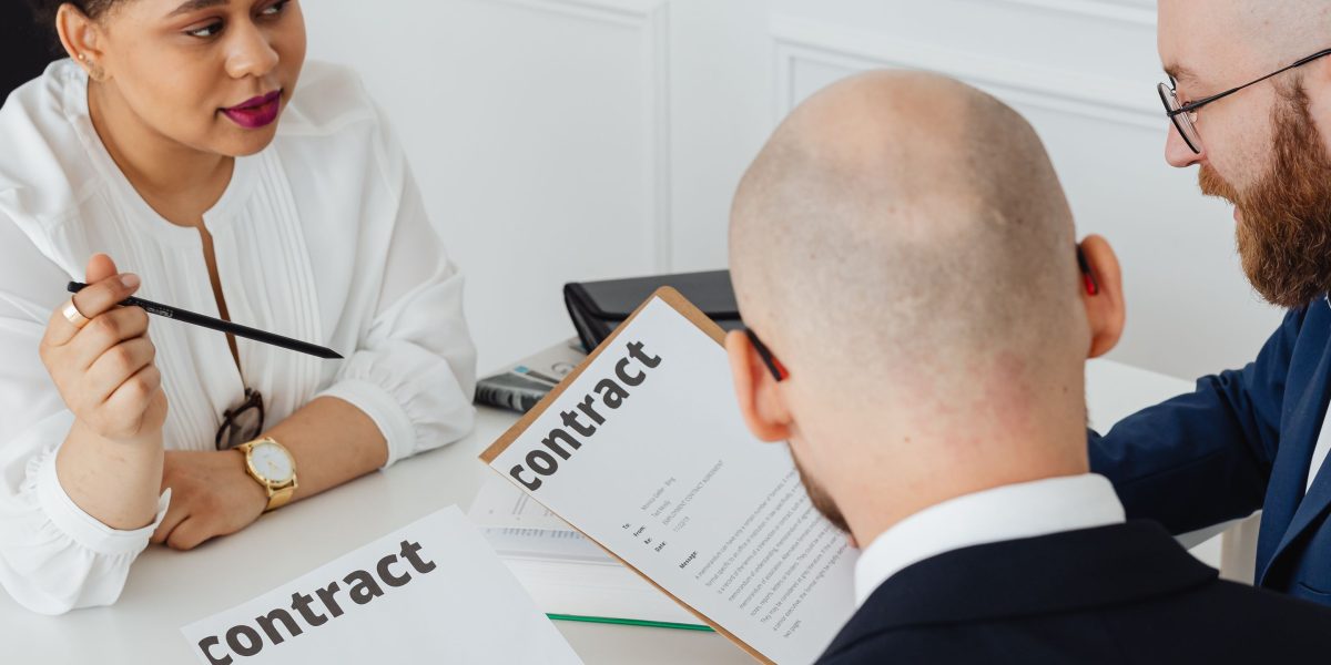 Individuals reviewing a contract document in a professional setting, emphasizing the importance of understanding terms.